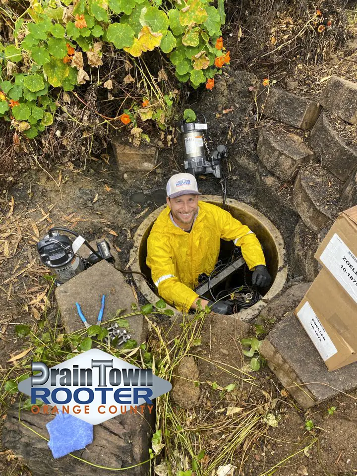 Drain Town Rooter plumber smiling while working inside an underground access pit